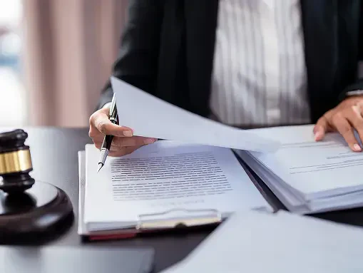 Person in business attire reviewing legal documents at a desk with a gavel nearby, suggesting a legal or court setting.