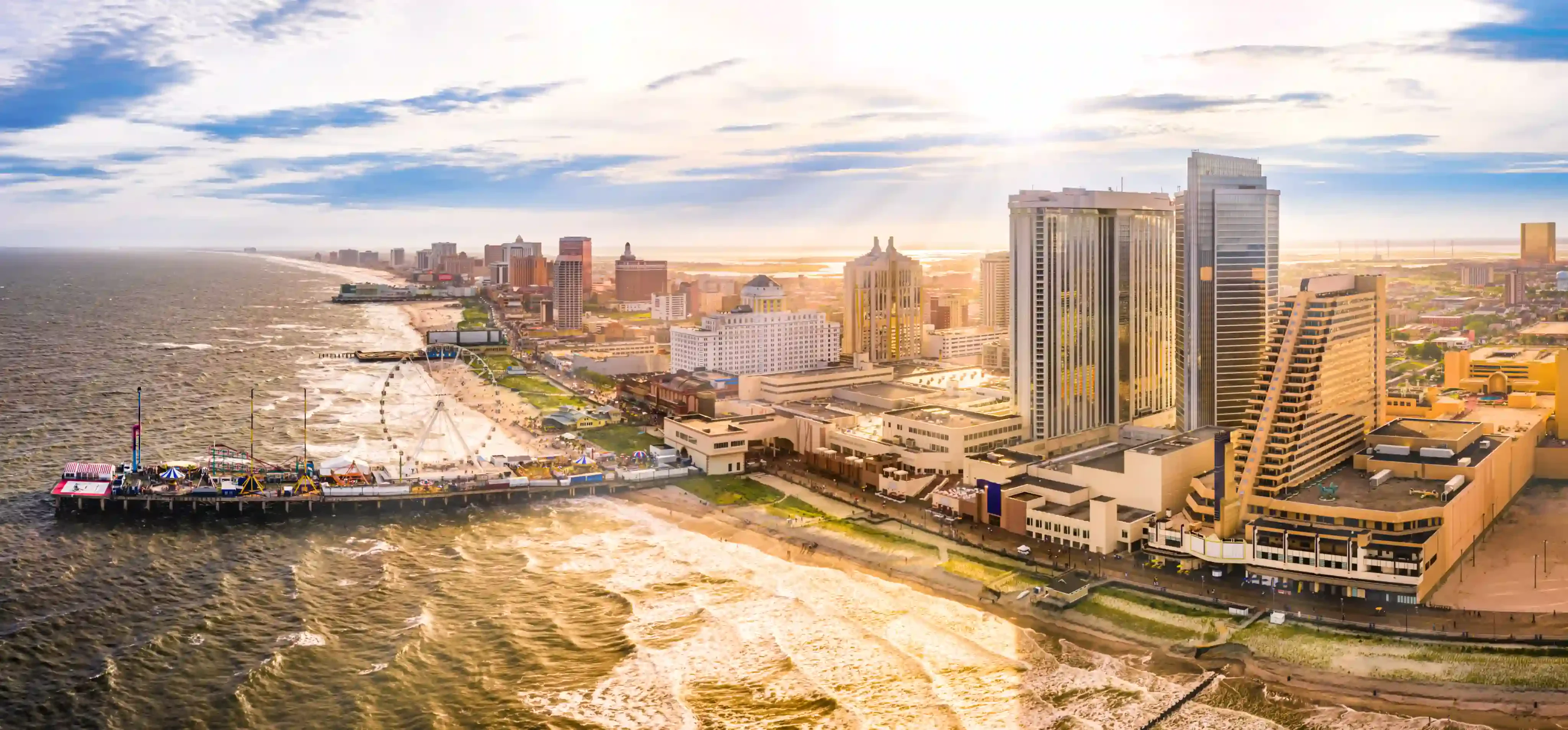 Aerial view of a coastal city with a long sandy beach, piers, and a skyline of high-rise buildings along the shore.